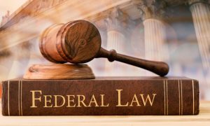 Federal Law Written on the Side of Book Sitting on Desk with Judge's Gavel and Courthouse Background