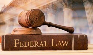 Federal Law Written on the Side of Book Sitting on Desk with Judge's Gavel and Courthouse Background
