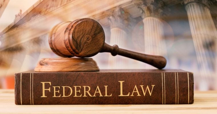 Federal Law Written on the Side of Book Sitting on Desk with Judge's Gavel and Courthouse Background