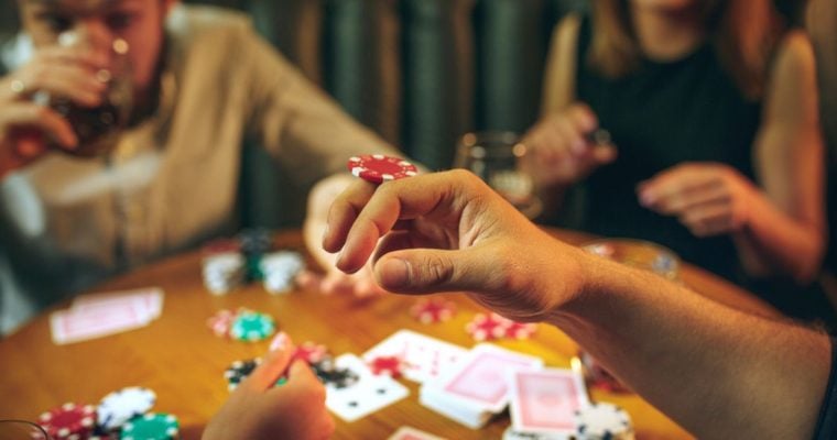 Three People Playing Poker with Foreground Image Closeup of Man Balancing Poker Chip on Hand