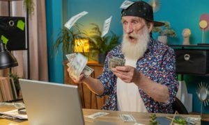Older Man Stares at Laptop in Shock with Cash Falling From Sky Around Him