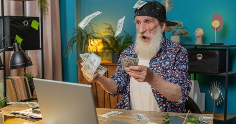 Older Man Stares at Laptop in Shock with Cash Falling From Sky Around Him