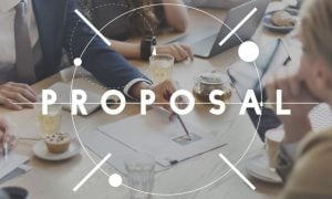 Team of Developers Sit at A Table Discussing Plans with Text Proposal Written Over Image