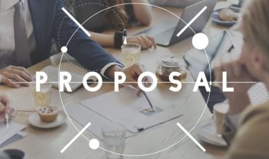 Team of Developers Sit at A Table Discussing Plans with Text Proposal Written Over Image