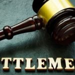 Judge's Wooden Gavel with Gold Trim Sits on Green Desk Above the Word Settlement