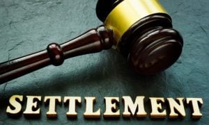 Judge's Wooden Gavel with Gold Trim Sits on Green Desk Above the Word Settlement
