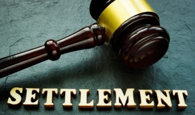 Judge's Wooden Gavel with Gold Trim Sits on Green Desk Above the Word Settlement