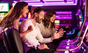 Bright Pink Lights of Slot Machines Shine While 3 Players Gambline Inside Casino