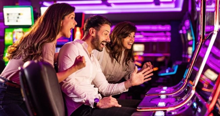 Bright Pink Lights of Slot Machines Shine While 3 Players Gambline Inside Casino