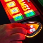 Close Up of Hand Pressing Play Button On Brightly-Lit Casino Slot Machine