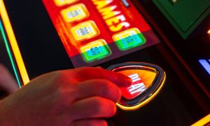 Close Up of Hand Pressing Play Button On Brightly-Lit Casino Slot Machine