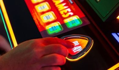 Close Up of Hand Pressing Play Button On Brightly-Lit Casino Slot Machine