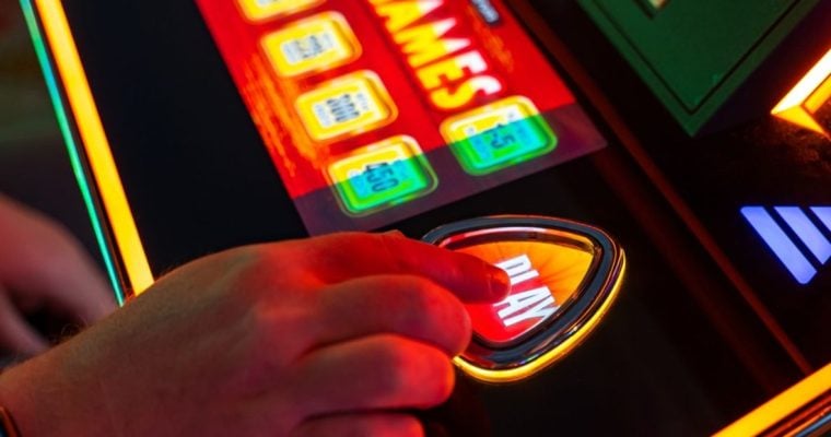 Close Up of Hand Pressing Play Button On Brightly-Lit Casino Slot Machine