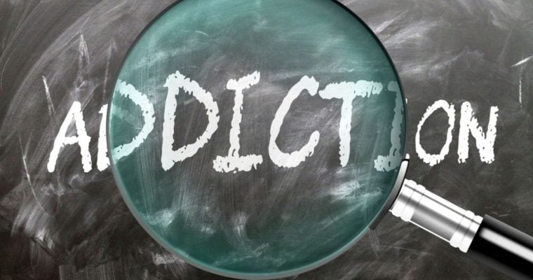 Magnifying Glass Sits on Blackboard with the Word Addiction Written