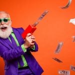 Man In Purple and Green Suit with Happy Expression Uses Money Rain Machine to Make Cash Fall from Air