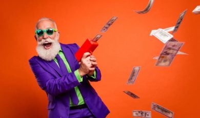 Man In Purple and Green Suit with Happy Expression Uses Money Rain Machine to Make Cash Fall from Air