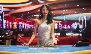 Dark-haired Asian Card Dealer Stands Behind Blackjack Table Inside Casino