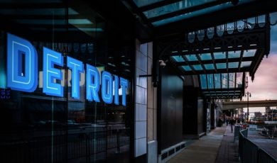 Commercial Building with Blue Neon Detroit Sign and People Walking Around at Sunset in Michigan