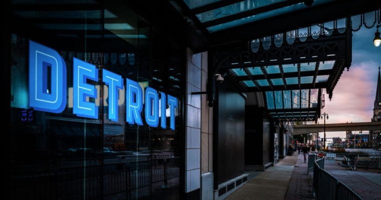 Commercial Building with Blue Neon Detroit Sign and People Walking Around at Sunset in Michigan