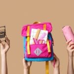Back-To-School Supplies Like Pink Backpack, Scissors and Pencil Case Held Up By Hands on Solid Background