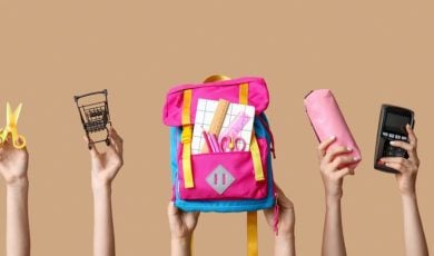 Back-To-School Supplies Like Pink Backpack, Scissors and Pencil Case Held Up By Hands on Solid Background