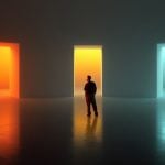 Man Stands In the Middle of Three Colorful Glowing Open Doors In Gray Room