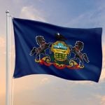 Blue Flag with Pennsylvania Crest Flies on Flag Pole Against Sunset Sky
