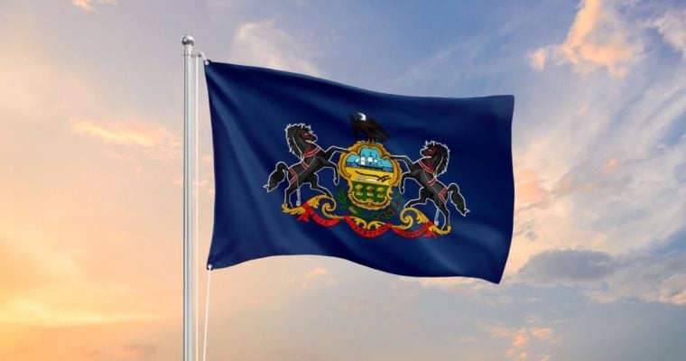 Blue Flag with Pennsylvania Crest Flies on Flag Pole Against Sunset Sky