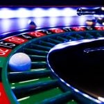 Close Up Image of Lit Roulette Wheel with White Ball Landed on Green 0