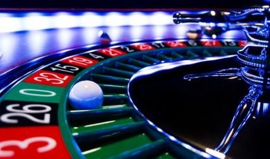 Close Up Image of Lit Roulette Wheel with White Ball Landed on Green 0