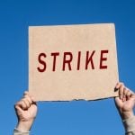 Hands Hold Up Cardboard Sign with Strike in Red Letters