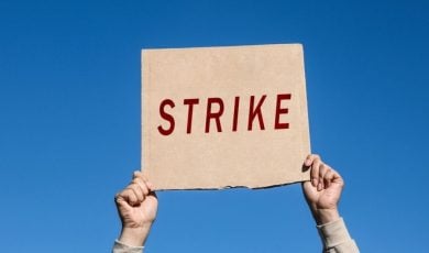 Hands Hold Up Cardboard Sign with Strike in Red Letters