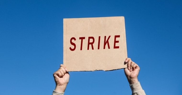Hands Hold Up Cardboard Sign with Strike in Red Letters