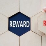 Word Reward Sits Underneath Wooden Block, Woman Holds Risk Piece