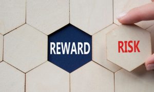 Word Reward Sits Underneath Wooden Block, Woman Holds Risk Piece