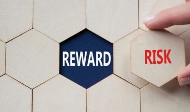 Word Reward Sits Underneath Wooden Block, Woman Holds Risk Piece