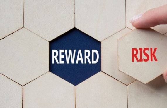 Word Reward Sits Underneath Wooden Block, Woman Holds Risk Piece