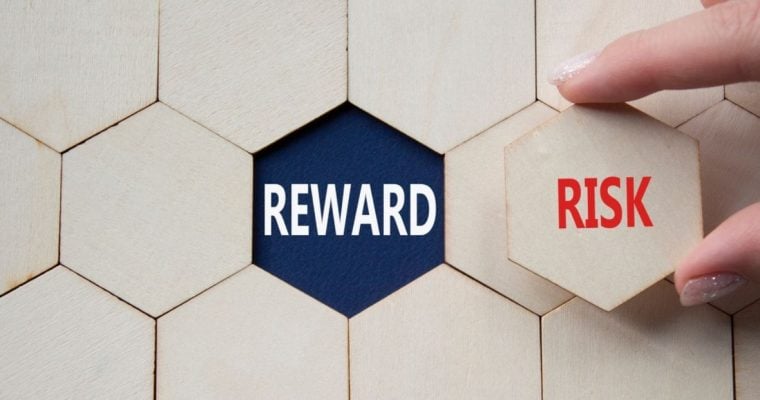 Word Reward Sits Underneath Wooden Block, Woman Holds Risk Piece