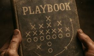 Man's Hands Hold Old Brown Playbook with Game Moves On Cover