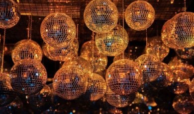 Disco Balls With Metallic Gold Glow Hang from Ceiling in Dark Background