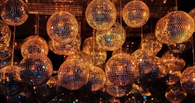 Disco Balls With Metallic Gold Glow Hang from Ceiling in Dark Background