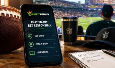 Man Watches Football Game in Background with DraftKings App on Cell Phone