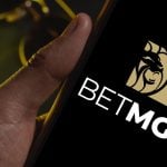 Men's Sunglasses and Gold Watch in Background to Man Holding Cell Phone with BetMGM Logo
