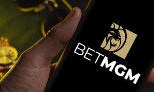Men's Sunglasses and Gold Watch in Background to Man Holding Cell Phone with BetMGM Logo