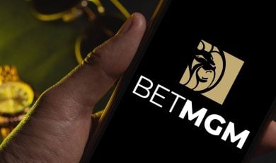 Men's Sunglasses and Gold Watch in Background to Man Holding Cell Phone with BetMGM Logo