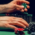 Man Uses Laptop to Play Online While Holding Colorful Poker Chips
