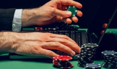 Man Uses Laptop to Play Online While Holding Colorful Poker Chips