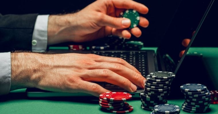 Man Uses Laptop to Play Online While Holding Colorful Poker Chips