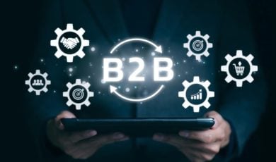 Digital Icons in White with Text B2B Hovers Over Tablet Held By Man in Dark Suit