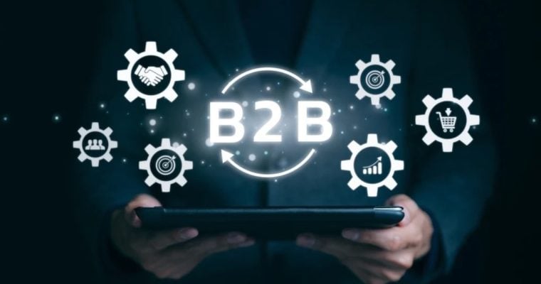 Digital Icons in White with Text B2B Hovers Over Tablet Held By Man in Dark Suit